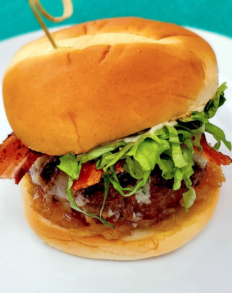 Close-up of a bacon cheeseburger with lettuce on a soft bun, served on a white plate.