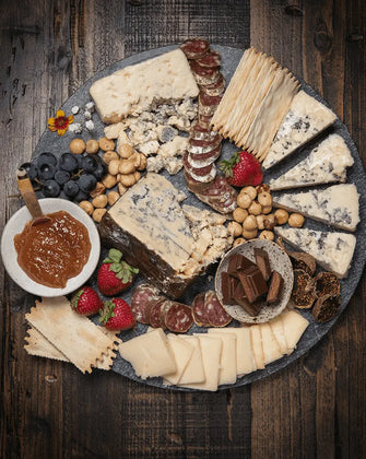 Organic cheese, james, crackers, salami, and fresh fruit on a marble cutting board