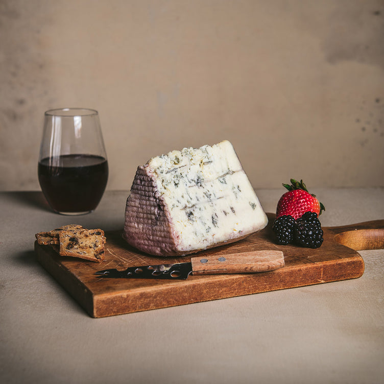 Organic red wine soaked blue cheese on cutting board with knife and crackers