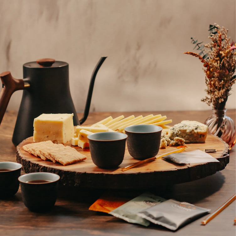 Organic Cheese on cutting board with honey sticks, tea packets, tea cups, and tea pot in the background