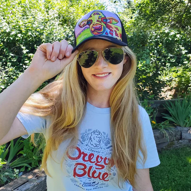 Person wearing a Rainbow Cow hat and sunglasses outdoors, showing the colorful cow design on the front of the cap.