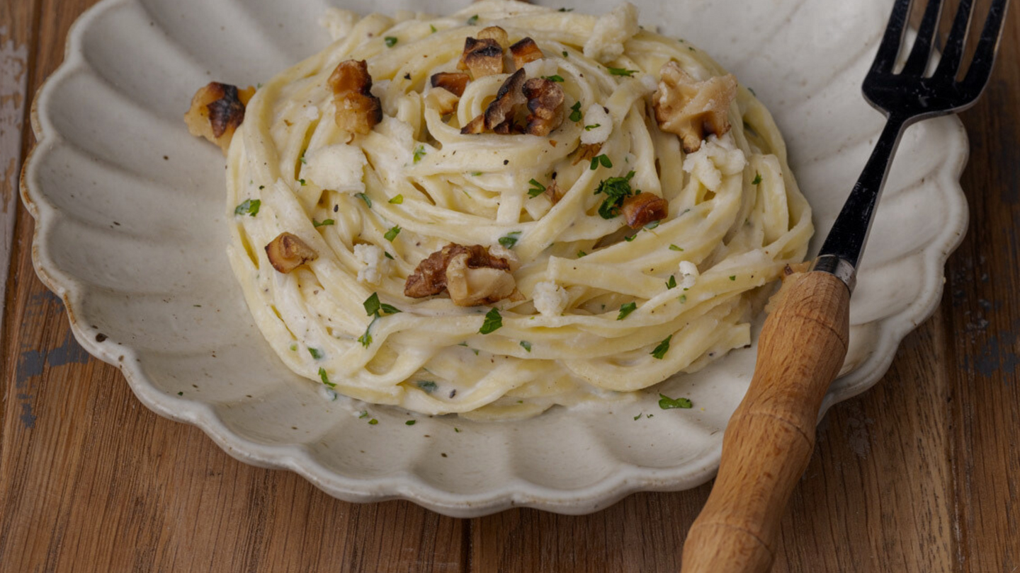 A plate of creamy pasta garnished with walnuts and herbs