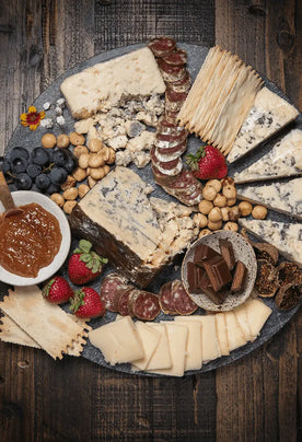 Organic cheese, james, crackers, salami, and fresh fruit on a marble cutting board