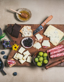 An assortment of cheese on a cutting obard with meat and honey