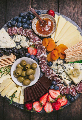 Organic cheeses, jams, chocolate, salmai, crackers, and fruit slices on a marble cuttingboard