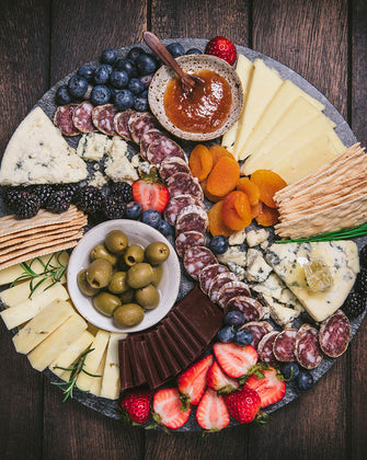 Organic cheeses, jams, chocolate, salmai, crackers, and fruit slices on a marble cuttingboard