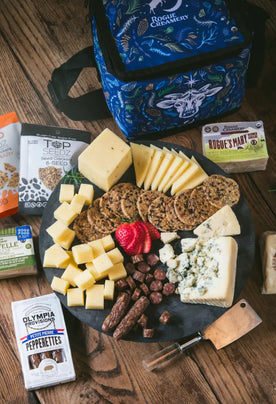 Organic cheeses, crackers, salami, and cooler back on wooden background