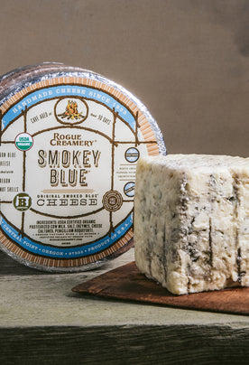 Organic Smokey Blue Cheese whole wheel with wedge on a cutting board