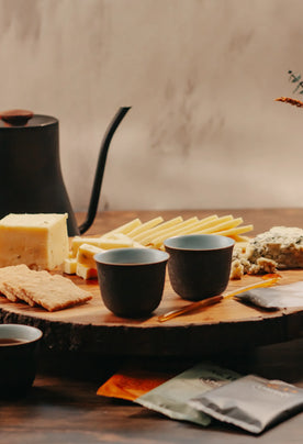 Organic Cheese on cutting board with honey sticks, tea packets, tea cups, and tea pot in the background