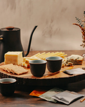 Organic Cheese on cutting board with honey sticks, tea packets, tea cups, and tea pot in the background