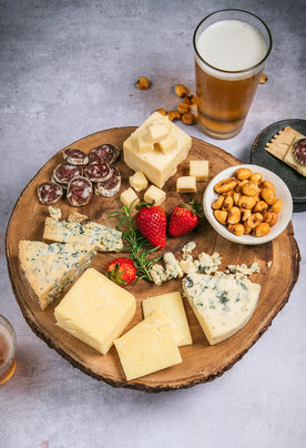 Organic cheeses with salami, beer, and corn nuts on cutting board