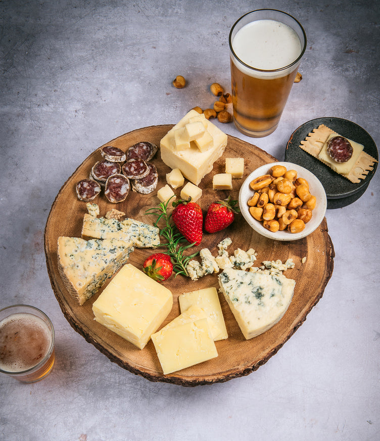 Organic cheeses with salami, beer, and corn nuts on cutting board