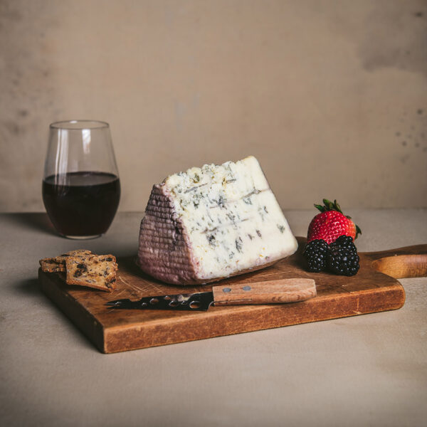 Rogue Creamery Bluehorn Red Wine Soaked Blue Cheese on cutting board with cheese knife and assorted fruit