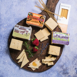 Rogue Creamery Cheddar Trio Gift Set on board with packaging, honey sticks, and fruit