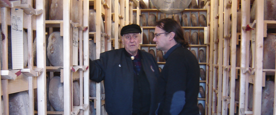 Two men looking at blue cheese wheels in cheese cave
