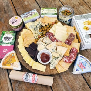 Organic Blue Cheeses and Cheddars piled onto a cheese board with jam, chocolate, olives, salami, and crackers.