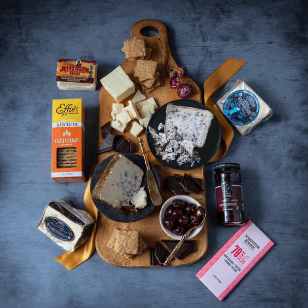 Rogue Creamery Winner's Circle Gift Set Contents including Chocolate, Oatcakes, Blue Cheese, and Cheddar Cheese on a cutting board