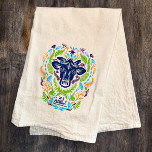 Rogue Creamery Floral Cow Tea Towel on wooden background